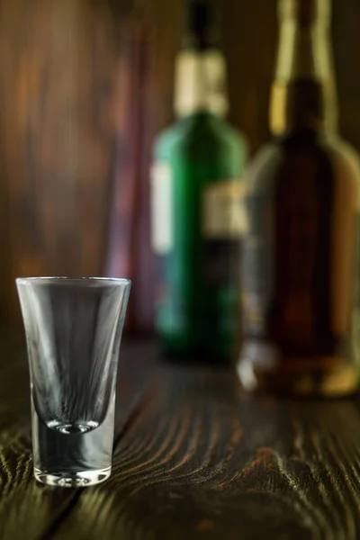 Un vaso de tequila vacío frente a muchas botellas de licor de colores, poca profundidad de campo, enfoque selectivo . — Foto de Stock