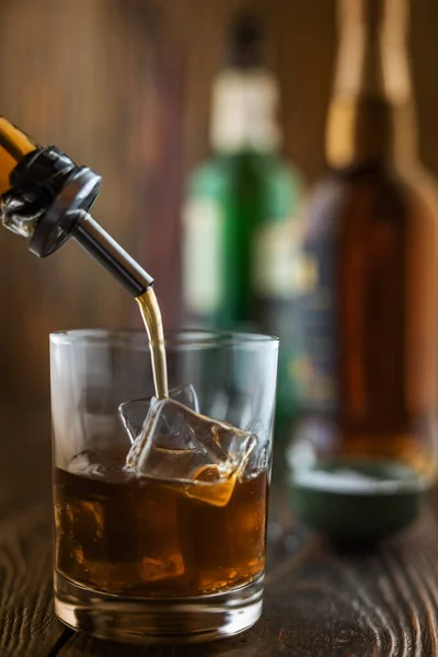 在酒吧里，威士忌倒入一个装有冰块的杯子里，在酒吧柜台的木制桌子上有瓶子，场地深度浅，有选择的焦点。酒精饮料的概念 — 图库照片