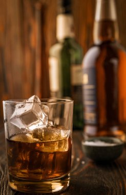 Arka planda buzlu bir bardak viski bir bar tezgahının ahşap masasında şişeler, sığ alan derinliği, seçici odaklanma. Yol kenarındaki bir barda alkollü içecekler konsepti.