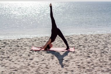Yoga yapan kadın sabah güneşinde plajda antrenman yapıyor. 