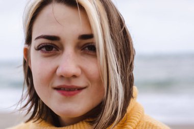 Sahilde sarı kazaklı güzel bir genç kadının portresi.