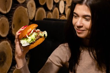 Hamburger yiyen, gülümseyen, aç genç bir kadının portresini yakından çek.