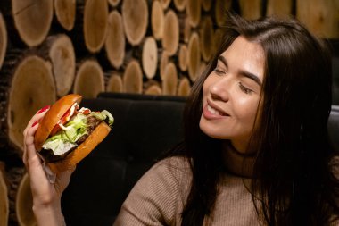 Hamburger yiyen, gülümseyen, aç genç bir kadının portresini yakından çek.