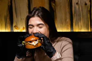 Hamburger yiyen, gülümseyen, aç genç bir kadının portresini yakından çek.