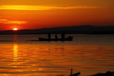 Ufukta Güneş 'in yanında parlak turuncu gökyüzü olan tek bir tekne..
