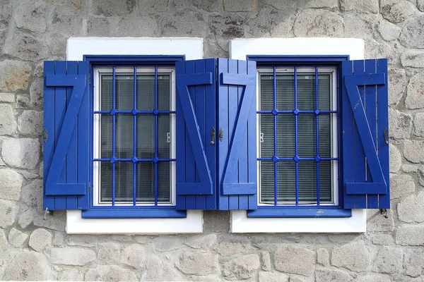 Mavi, açık ahşap pencere panjurları ve Akdeniz evlerinin kırsal duvarlarının detaylı görüntüsü