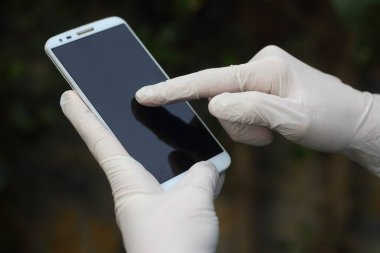 Akıllı telefonunu kullanırken lateks eldiven takan genç bir adamın yakın çekimi.