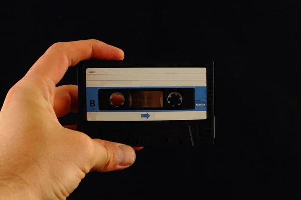 one old audio cassette is on a hand on a blue background