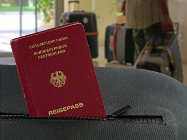 Arka planda otel lobisi olan siyah bir valizin cebinde Alman pasaportu.