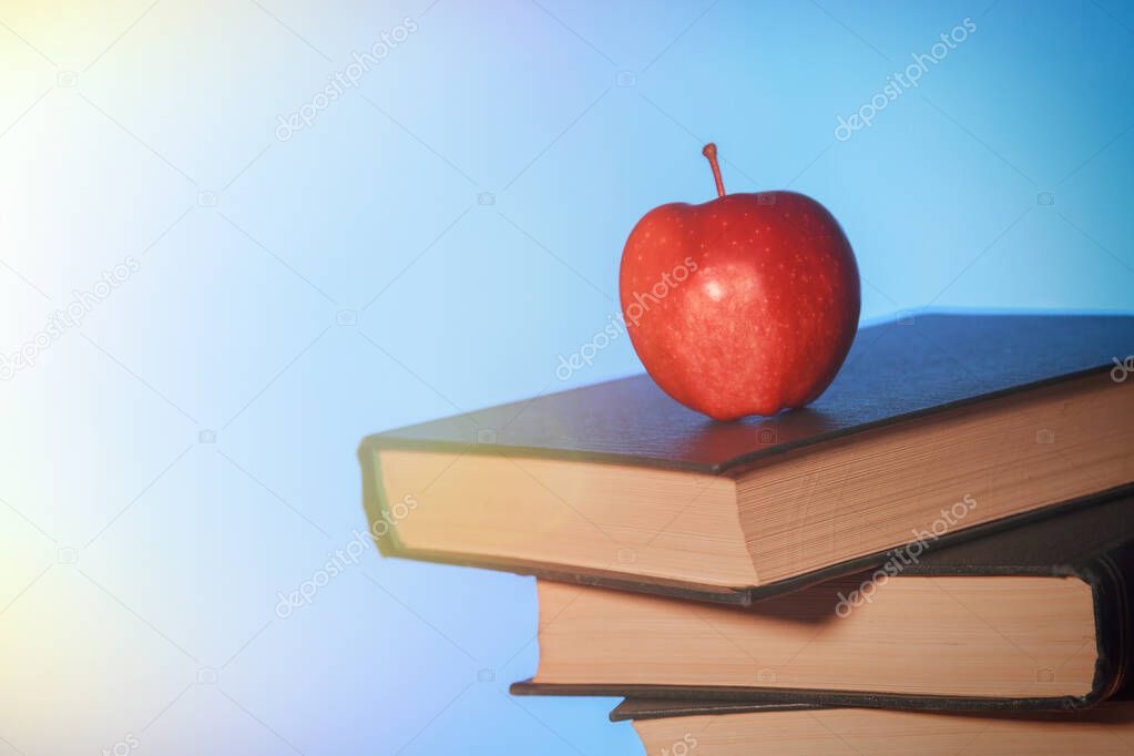Red apple on a pile of old books on a desk.