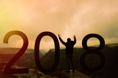 2018 'de dağın tepesinde duran bir adamın silueti. Ve bir kazanan gibi iki elini birden uzattı. 