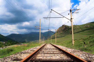 Çevresinde yeşil çimenler ve dağlar olan tren istasyonu.. 