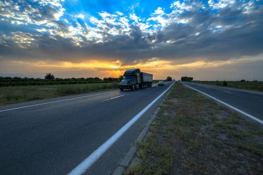 Büyük bir kamyon ve bir araba muhteşem bir dramatik gün batımında yolda.. 
