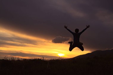 Gün batımında zıplayan bir çocuğun silueti..