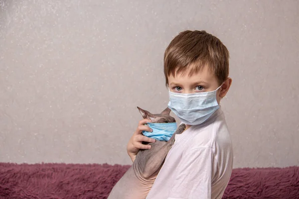 Un niño y un gato calvo con máscaras médicas se protegen del virus, coronavirus, epidemia, contaminación del aire — Foto de Stock