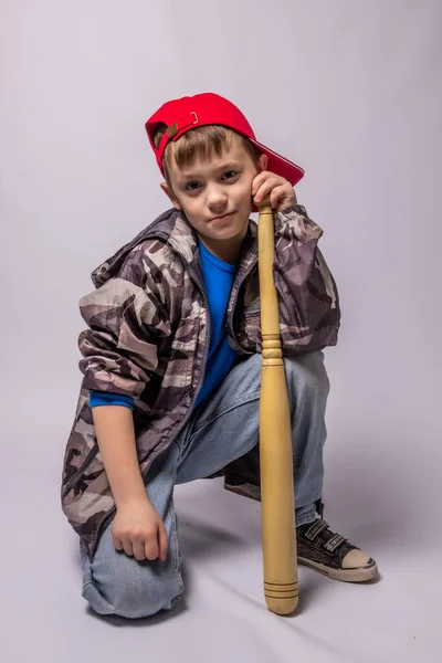 Child boy in jeans and a protective jacket in a red cap with a bat on a white background — Stock Photo, Image