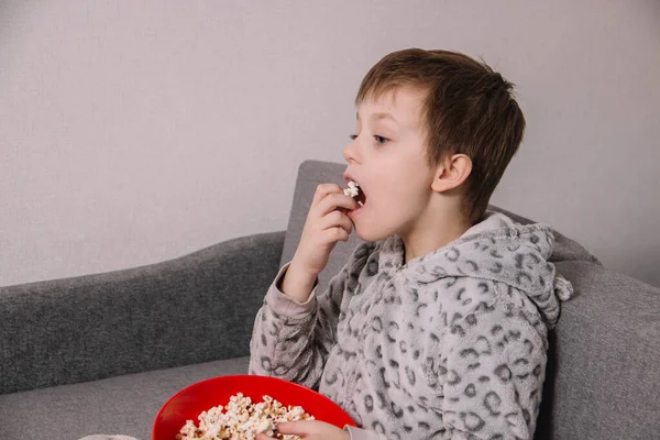 A guy sits on a couch and eats popcorn in isolation while watching a movie or cartoon
