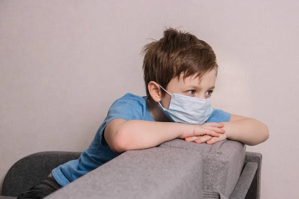 Trauriges Baby Blauem Shirt Und Medizinischer Maske Auf Dem Sofa lizenzfreie Stockbilder