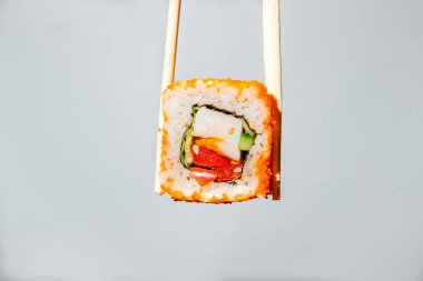 Beyaz arka planda çubuklarla tutulan bir suşi rulosu, yakın plan.