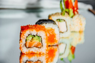 Aynalı bir masaya serilmiş güzel suşi, yansıma görünür, arka plan bulanık.