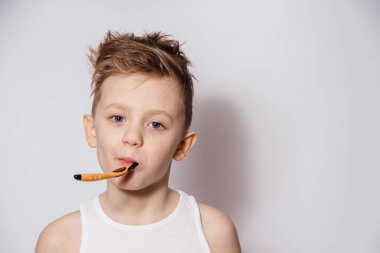 Çocuk beyaz arka planda bir diş fırçasıyla dişlerini dikkatlice fırçalar.
