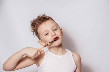 Çocuk beyaz arka planda bir diş fırçasıyla dişlerini dikkatlice fırçalar.