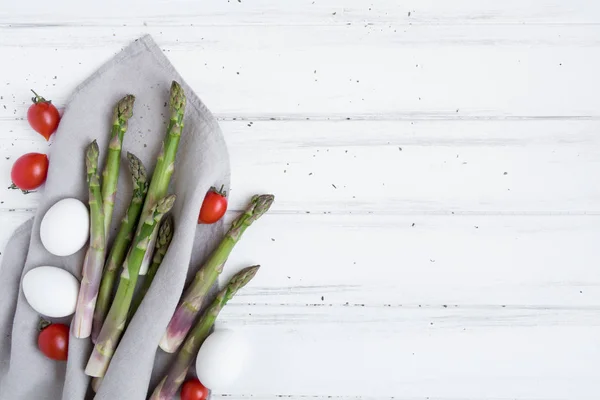 Ingredienti per una sana colazione: asparagi freschi, pomodori, uova sul tavolo bianco. Composizione in stile rustico. Posa piatta, vista dall'alto — Foto Stock