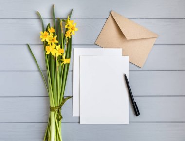 Mektup, zarf ve Nergis gri arka plan üzerinde. Romantik tatil kavramı, üstten görünüm, düz yatıyordu