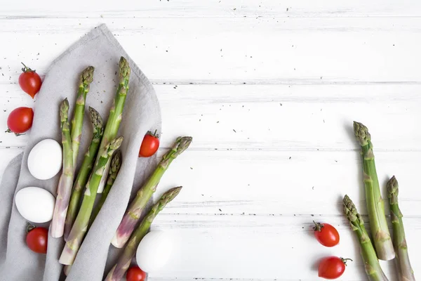 Ingredienti per una sana colazione: asparagi freschi, pomodori, uova sul tavolo bianco. Composizione in stile rustico. Posa piatta, vista dall'alto — Foto Stock