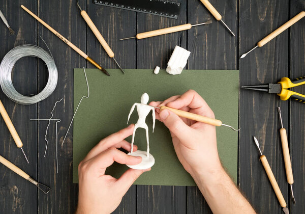Craftsman hands working on human sculpture, sculpturing from polymer clay against working table with tools. Flat lay, top view