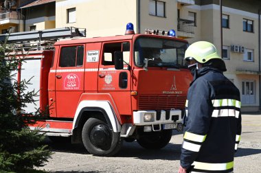 İtfaiyeci kasklı, itfaiye arabasının yanında.