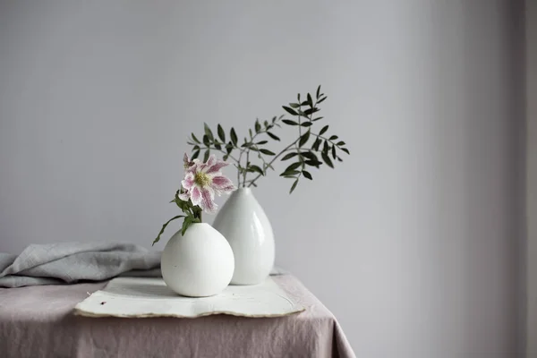 Flores de lirio rosado y ramas de plantas follaje en jarrones en la mesa — Stock Photo