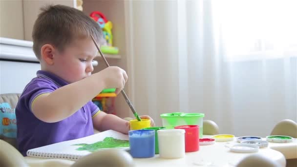 Niño dibuja con pinturas de colores mientras está sentado en la mesa — Vídeos de Stock