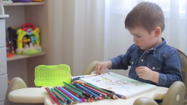 Een klein kind leert tekenen met kleurpotloden op papier — Stockvideo