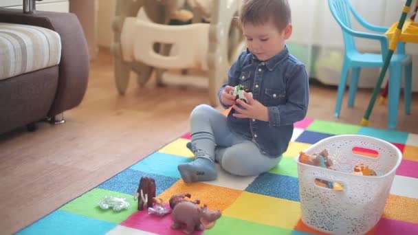 De kleine jongen zit op de vloer en speelt met verschillende dieren — Stockvideo