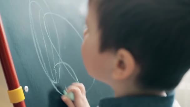 Küçük bir çocuk bir tahtaya tebeşir çizmeyi öğrenir — Stok video