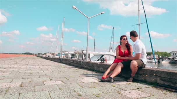 Junges Mädchen in rotem Kleid und ihr Freund sitzen auf dem Pier — Stockvideo