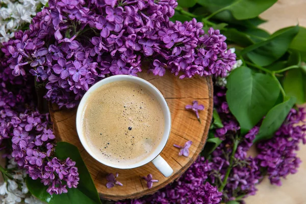 spring background. coffee stands on a wooden hemp surrounded by lilac flowers