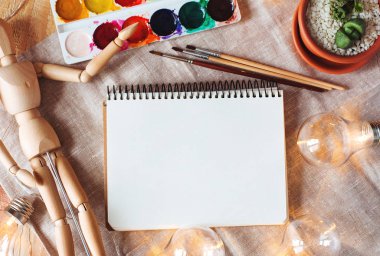 Üstten Görünüm mockup not defteri, boyalar, fırçalar, çiçek, ahşap kukla ve ampul ahşap ve kumaş arka plan üzerinde. Hazır metin eklemek için.