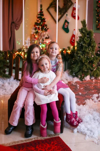 Noel süsleri içinde gülümseyen ve sarılan üç kız.