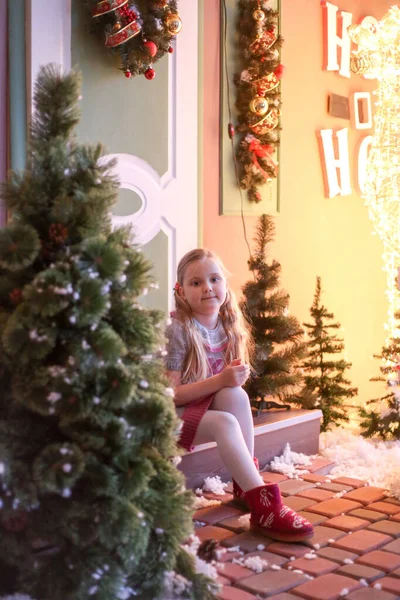 Yeni yıl süslemeleriyle kapının eşiğinde oturan küçük kız.