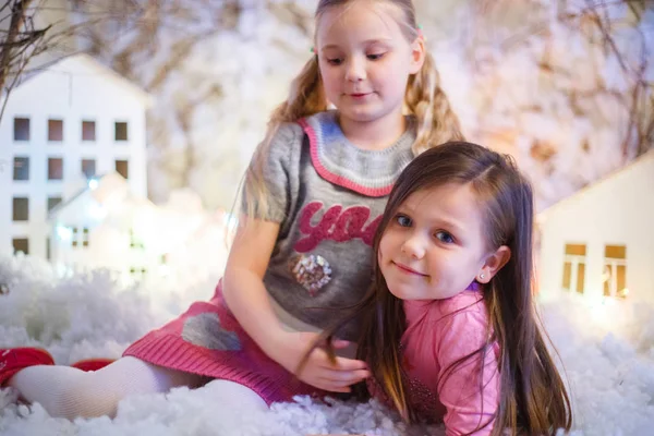 Yapay kar ve küçük karton evlerle Noel süslemeleri yapan iki kız.