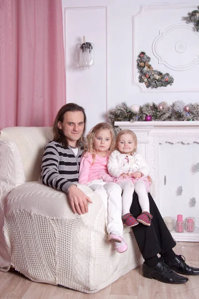 お正月飾りの暖炉のそばで椅子に座っていた2人の娘を持つ父 — ストック写真