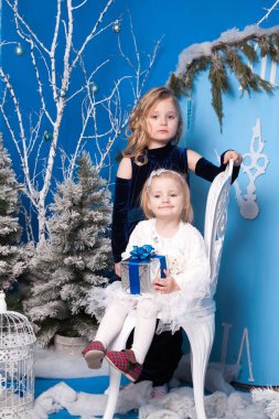 Yapay bir Noel ağacı ve büyük bir yapay saatin yanındaki kış manzarasında iki kız.