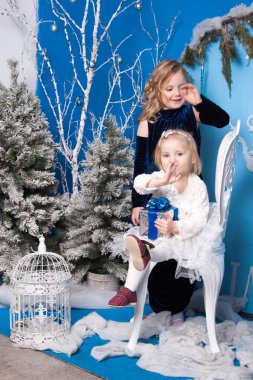 Yapay bir Noel ağacı ve büyük bir yapay saatin yanındaki kış manzarasında iki kız.