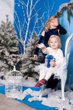 Yapay bir Noel ağacı ve büyük bir yapay saatin yanındaki kış manzarasında iki kız.