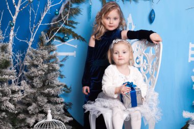 Yapay bir Noel ağacı ve büyük bir yapay saatin yanındaki kış manzarasında iki kız.