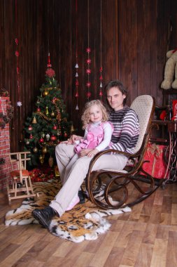 Baba ve kollarında küçük bir kızı sallanan bir sandalyede oturuyor.