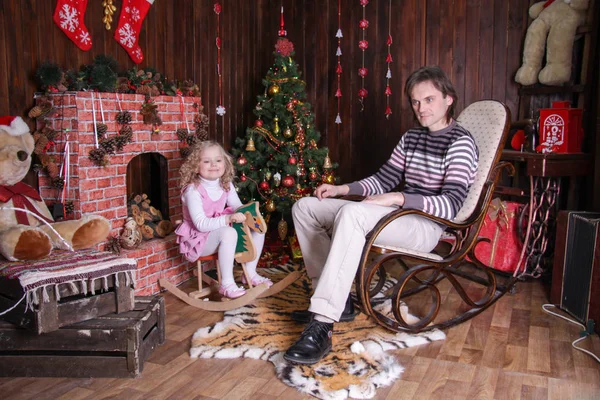 パパはロッキングチェアに座って娘は新年の飾りの馬に座って — ストック写真