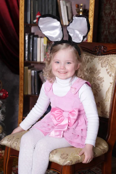 Tavşan kulaklı küçük kız sandalyede oturuyor.